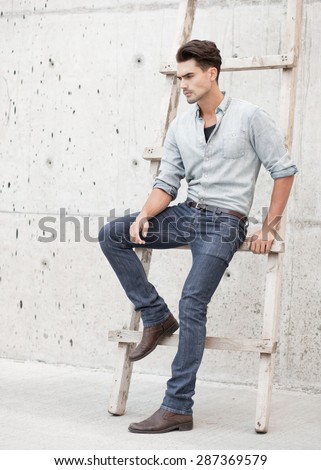 Handsome man dressed in a blue jeans shirt, jeans and a cap, posing