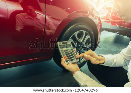 This career salesman calculating on calculator car price in showroom\
car.Close up tire red car in dealership transport automobile industry\
inspection business automotive