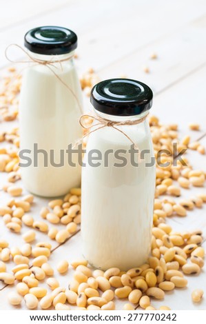 Soy milk [Soya milk ] in  glass bottle with soy pods on white wooden background, healthy drink