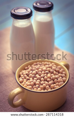 Soy milk [Soya milk ] in glass bottle with soy pods on white wooden background, healthy drink