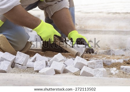 Man kneeling at work, street worker, paving with hammer in yellow gloves.