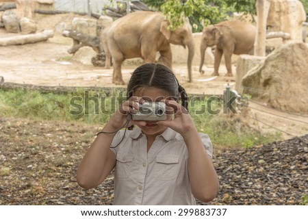 Young photographer, portrait of little girl taking photos in the zoo at the elephants.