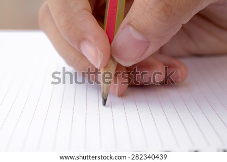 Close-up of hand pencil writes in a notebook