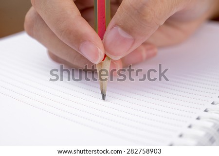Close-up of hand pencil writes in a notebook