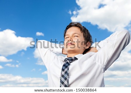 Boy in white shirt and a tie, his hands behind his back, his eyes are closed, face upwards looking happy, satisfied and relaxed. He is outside, with background a beautiful blue sky and white clouds