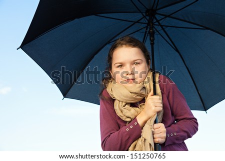 A little girl holding her umbrella  and she is cuddled underneath, she looks like as if she is cold.