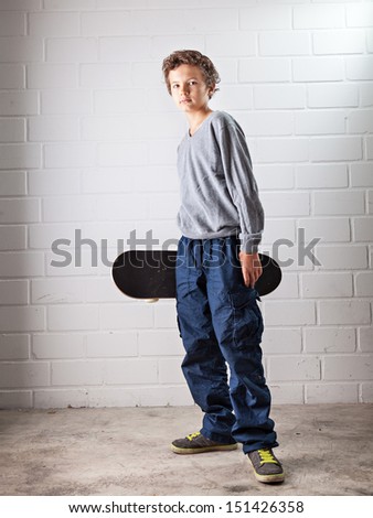 A Teenage boy, standing, his skateboard in his right hand, he is laughing