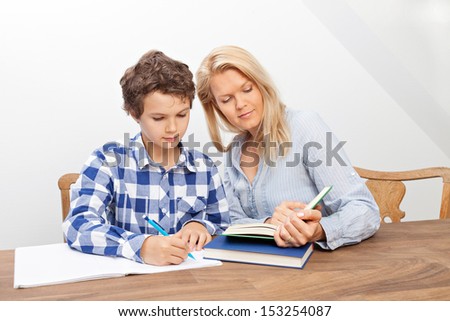 A boy is doing his homework and his mother is helping him with it. They look very happy.