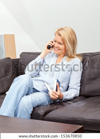 A beautiful blond woman is sitting on a couch, talking into the phone, having a conversation.