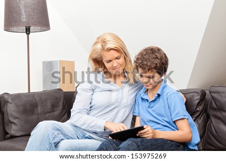 A beautiful woman and her teenage son at home, sitting on a couch reading on a tablet.