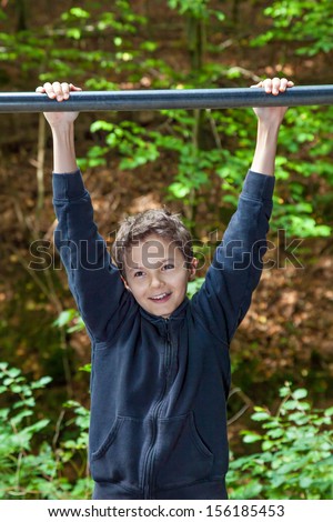 Charming Teenage boy in a forest, hanging on his arms from a chin up bar.