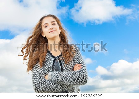 Teenage Girl with beautiful long curly hair. She is standing outside. Blue sky and clouds as background.