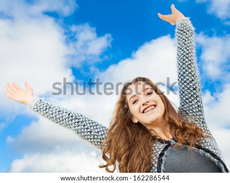 Teenage Girl with beautiful long curly hair, arms up in the air, she looks very happy.