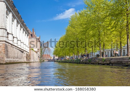 BRUGES, BELGIUM - APRIL 17, 2014: A low angle view on to the canal of Bruges. Next to the canal is a little park with people walking in the shadow