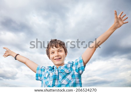 Portrait of a charming and very happy teenage Boy outside against cloudy sky - his arms up in the air