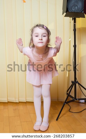 Little girl wearing a ballet dress is practicing ballet in a dance studio
