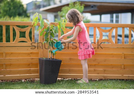 Happy little girl watering plants in the garden
