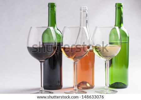 Three wine glasses and bottles with different wines - red, rose and white on a solid bright background