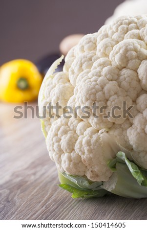 Close up photo of edible vegetables - a cauliflower with some vegetables in the background on a solid  brown wooden table