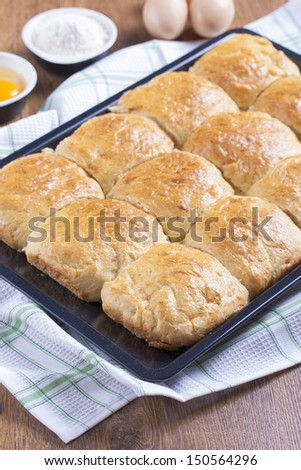 Fresh baked wheat rolls in black sheet tray on a white dish towel