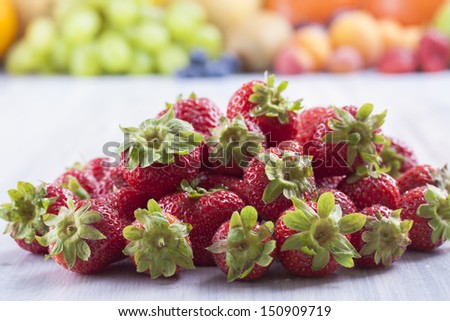 Close up photo of edible fruits - a strawberries with other full color fruits in the background on a solid  bright blue wooden table