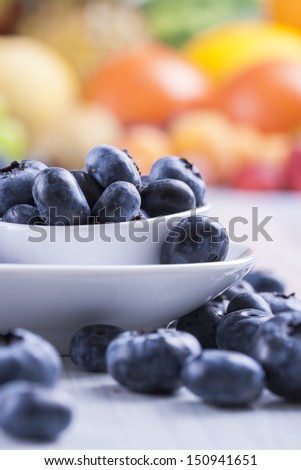 Close up photo of edible fruits - a blueberries with other full colors fruits in the background on a solid  bright blue wooden table