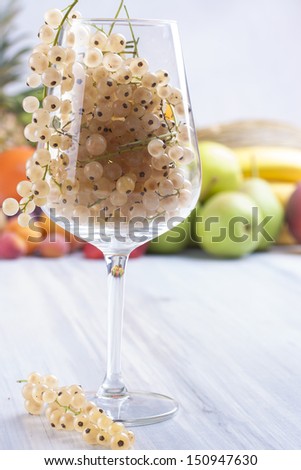 Close up photo of edible fruits - a white currant in the wine glass with other full colors fruits in the background on a solid  bright blue wooden table