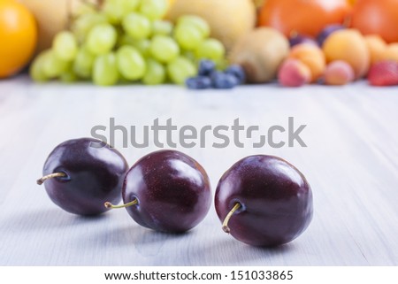 Close up photo of edible fruits - a sloes with other full colors fruits in the background on a solid  bright blue wooden table