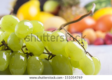 Close up photo of edible fruits - a green grapes with other full colors fruits in the background on a solid  bright blue wooden table