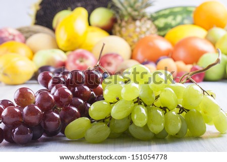 Close up photo of edible fruits - a red and green grapes with other full colors fruits in the background on a solid  bright blue wooden table