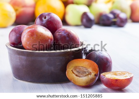 Close up photo of edible fruits - a plums with other full colors fruits in the background on a solid  bright blue wooden table