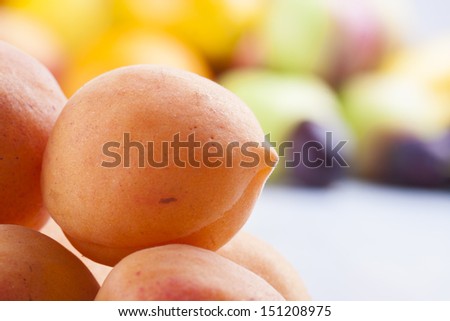 Close up photo of edible fruits - a plums with other full colors fruits in the background on a solid  bright blue wooden table