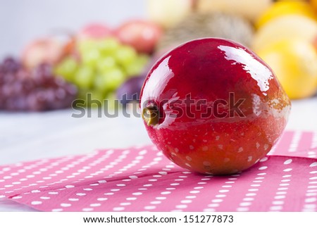 Close up photo of edible fruits - a mango with other full colors fruits in the background on a solid  bright blue wooden table