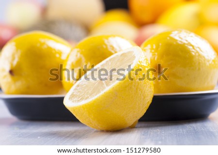 Close up photo of edible fruits - a lemons with other full colors fruits in the background on a solid  bright blue wooden table