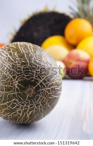 Close up photo of edible fruits - a melon with other full colors fruits in the background on a solid  bright blue wooden table