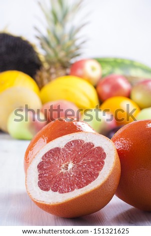 Close up photo of edible fruits - a grapefruit with other full colors fruits in the background on a solid  bright blue wooden table