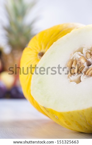 Close up photo of edible fruits - a yellow melon with other full colors fruits in the background on a solid  bright blue wooden table.