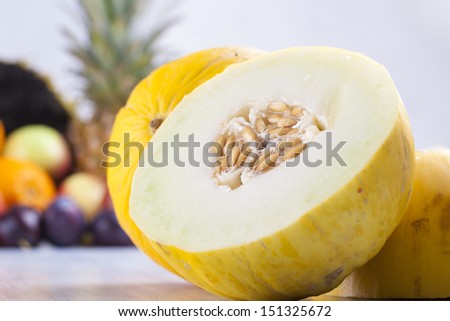 Close up photo of edible fruits - a yellow melon with other full colors fruits in the background on a solid  bright blue wooden table.