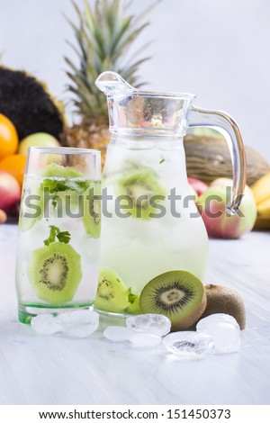 Fresh fruit and water drink with a green kiwi slices, mint herb and ice cubes with some fruits in the background.