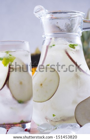 Fresh fruit and water drink with a red pears slices, mint herb and ice cubes with some fruits in the background.