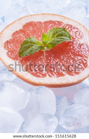 Composition of fresh red grapefruit slices with ice cubes and mint herb leaf.