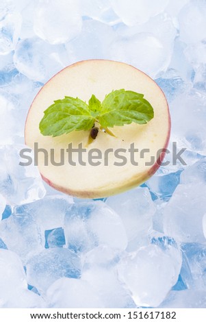 Composition of fresh red apple fruit slices with ice cubes and mint herb leaf.