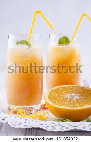 Glass of homemade fresh mixed orange fruits cocktail with water, ice cubes and mint herb leafs at the top.