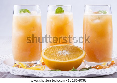 Glass of homemade fresh mixed orange fruits cocktail with water, ice cubes and mint herb leafs at the top.