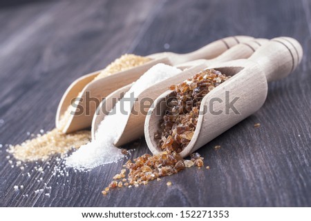 Close up photo of different kind of sugar - sugarcane, white and brown sugar in a spatula on a dark solid wooden background.