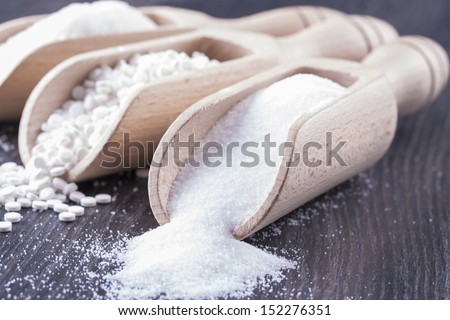 Food ingredients - sugar, aspartame and salt on a dark solid wooden background.