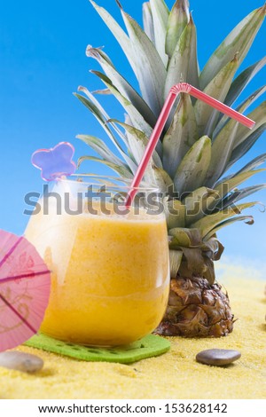 Close up photo of summer cocktail - mixed pineapple drink on a sand and blue background.