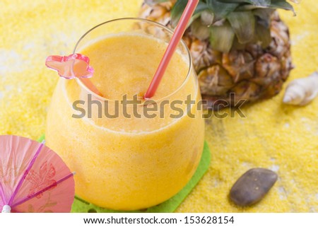 Close up photo of summer cocktail - mixed pineapple drink on a sand and blue background.