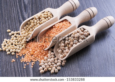 Close up photo of a raw food - orange seeds - red lentil, brown seeds - chickpeas, yellow beans - soybeans placed on a dark wooden background.