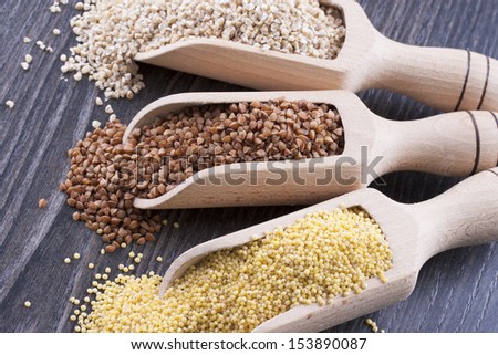 Close up photo of a eco raw food in the spoon - light brown pearl barley, dark brown kasha and yellow millet on a dark wooden background.